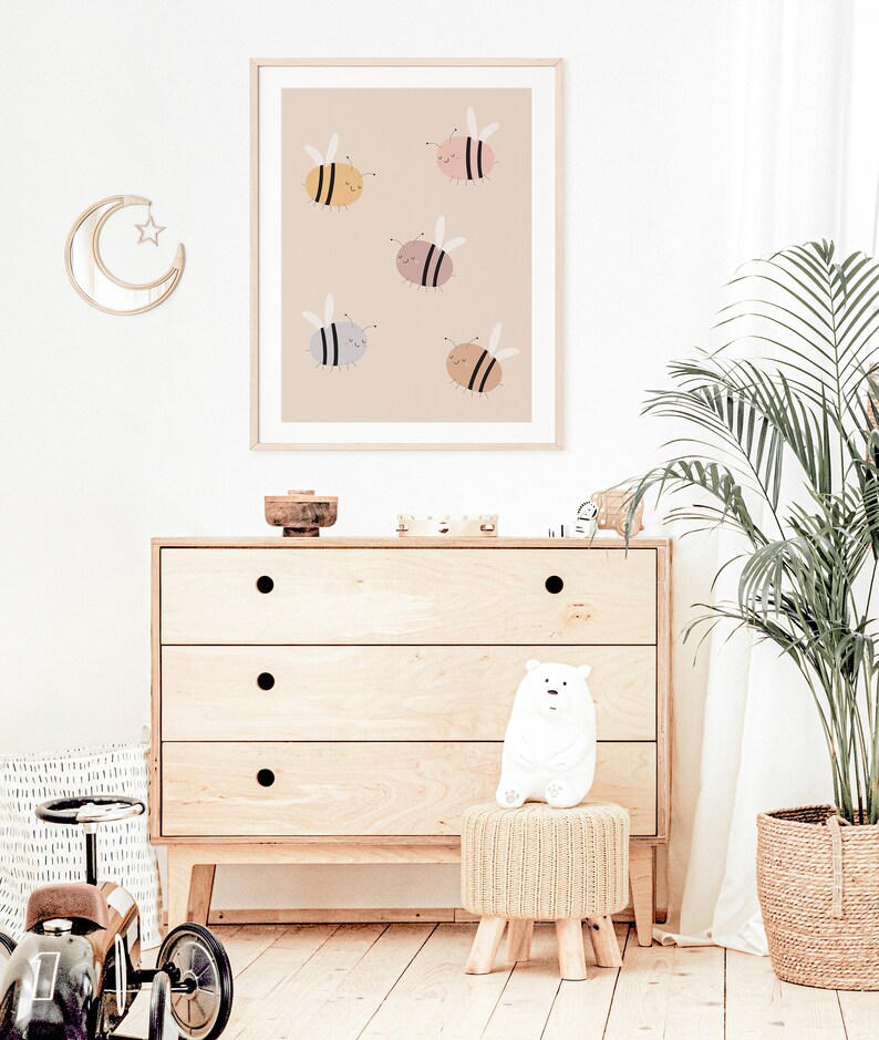Puede incluir: Una impresi&oacute;n enmarcada beige con un fondo marr&oacute;n claro que presenta cinco abejas de dibujos animados en varios colores, incluyendo amarillo, rosa, gris y marr&oacute;n. Las abejas est&aacute;n volando y tienen expresiones felices.
