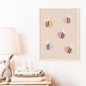 Puede incluir: Una impresi&oacute;n enmarcada con un fondo beige que presenta cinco abejas de dibujos animados en diferentes colores: amarillo, rosa, gris, marr&oacute;n claro y marr&oacute;n oscuro. Cada abeja tiene rayas negras y una cara sonriente.