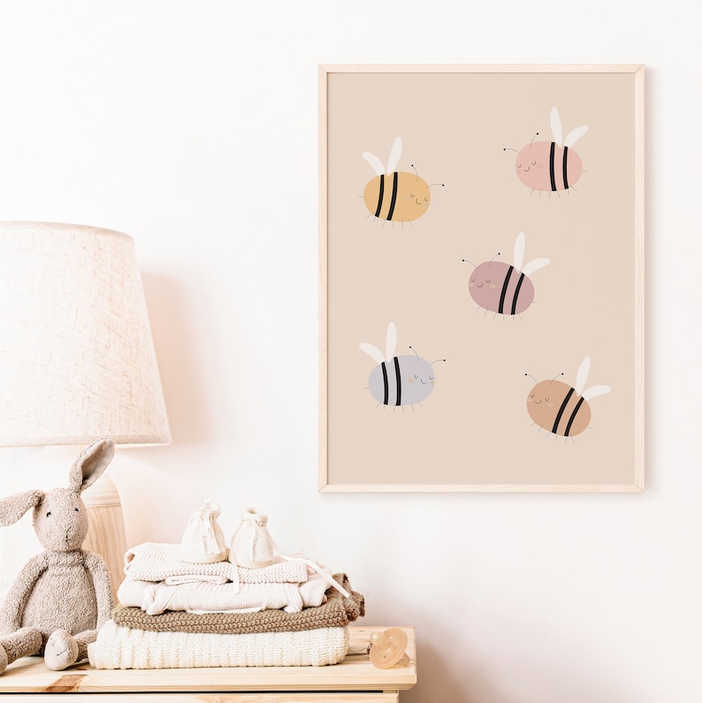 Puede incluir: Una impresi&oacute;n enmarcada con un fondo beige que presenta cinco abejas de dibujos animados en diferentes colores: amarillo, rosa, gris, marr&oacute;n claro y marr&oacute;n oscuro. Cada abeja tiene rayas negras y una cara sonriente.