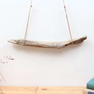 May include: A piece of driftwood is suspended from the ceiling by two pieces of twine. The driftwood is light brown and has a natural, weathered look.