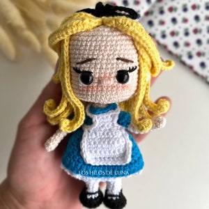 Puede incluir: Mu&ntilde;eca de ganchillo hecha a mano de Alicia en el pa&iacute;s de las maravillas, con un vestido azul, un delantal blanco y cabello rubio. La mu&ntilde;eca tiene zapatos negros y un lazo negro. El texto "LOS HILOS DE LUNA" es visible.