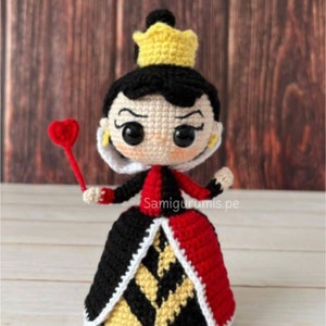 Pode incluir: Boneca amigurumi de croch&ecirc; da Rainha de Copas de Alice no Pa&iacute;s das Maravilhas. A boneca est&aacute; vestindo um vestido vermelho e preto com uma coroa amarela e segurando um cetro vermelho em forma de cora&ccedil;&atilde;o.