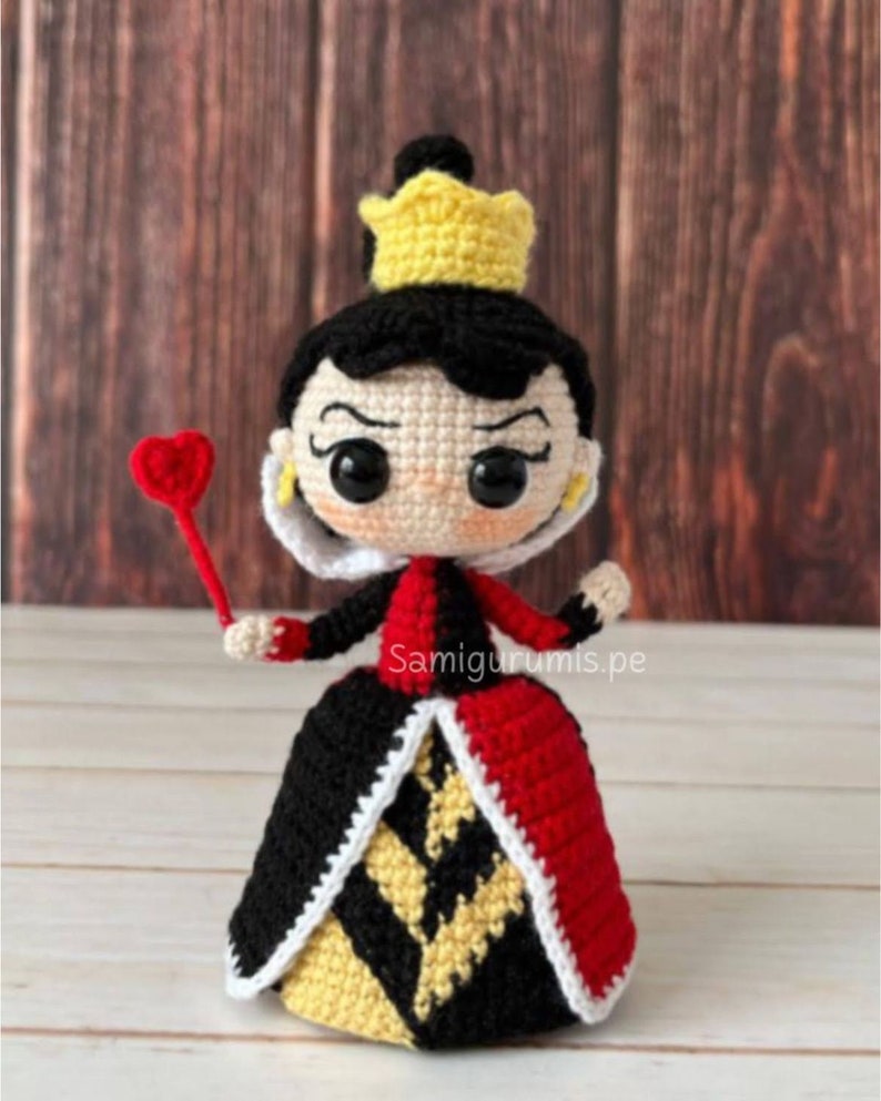 Pode incluir: Boneca amigurumi de croch&ecirc; da Rainha de Copas de Alice no Pa&iacute;s das Maravilhas. A boneca est&aacute; vestindo um vestido vermelho e preto com uma coroa amarela e segurando um cetro vermelho em forma de cora&ccedil;&atilde;o.
