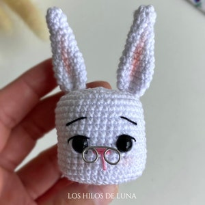 May include: A handmade white crochet bunny head with black eyes, a pink nose, and wire-rimmed glasses. The bunny has long ears with pink accents. The text "LOS HILOS DE LUNA" is at the bottom.