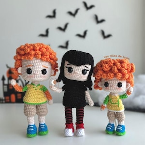 May include: Three crocheted amigurumi dolls, two with orange hair and one with black hair. The dolls are wearing colorful clothing and have big eyes. The dolls are standing on a white surface. The text "Los Hilos de Luna" is visible in the background.