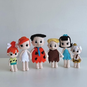 May include: A set of seven crocheted figures of the Flintstones family. The figures are all standing and are made in a variety of colours, including orange, brown, white, blue, and green.