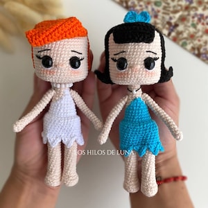 Puede incluir: Dos muñecas de crochet, una con pelo naranja y un vestido blanco, la otra con pelo negro y un vestido azul. Las muñecas se toman de la mano y tienen ojos grandes. El texto "LOS HILOS DE LUNA" es visible en la parte inferior de la imagen.
