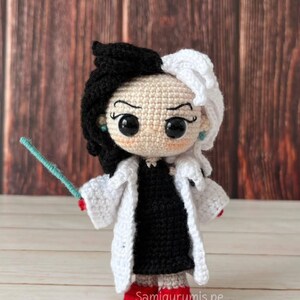 Pode incluir: Boneca de croch&ecirc; da Cruella de Vil do filme 101 D&aacute;lmatas da Disney. A boneca est&aacute; usando um vestido preto, um casaco branco e sapatos vermelhos. Ela tem cabelo preto e branco e est&aacute; segurando uma varinha azul.