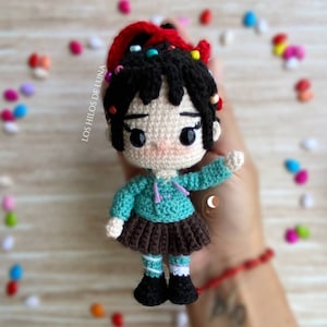 May include: A crocheted doll with black hair, a teal sweater, a brown skirt, and white and black shoes. The doll has a red and white hair bow with colorful beads.