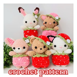 May include: Five crocheted stuffed animals wearing strawberry-themed outfits. The animals are a bunny, a cat, a bear, a fox, and a dog. The animals are all wearing red, pink, and green.