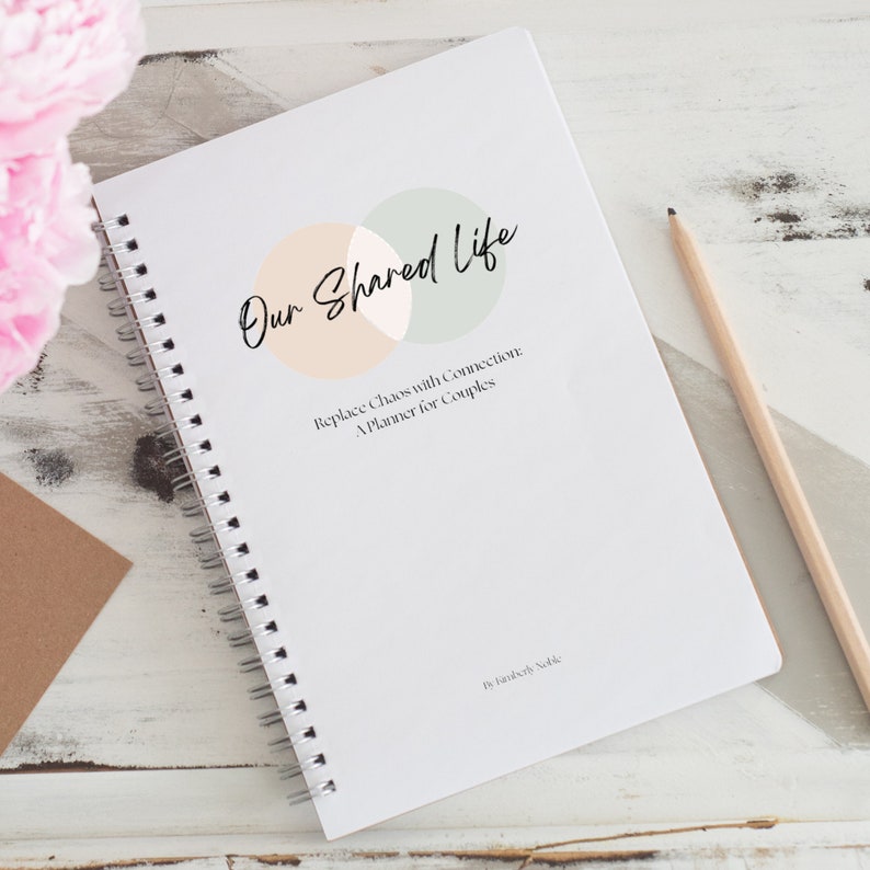 Op de afbeelding: Een wit spiraalgebonden notitieboek met de titel "Our Shared Life: Replace Chaos with Connection: A Planner for Couples" en een afbeelding van twee overlappende cirkels in perzik en groen. De tekst "By Honestly, Sadie" staat onderaan de pagina.