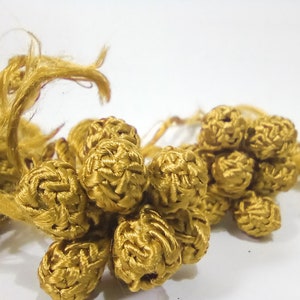 Op de afbeelding: Een cluster van gouden, gecrochete kwastjes met lange, rafelige uiteinden. De kwastjes zijn gemaakt van een zacht, getextureerd garen en hebben een delicate, handgemaakte uitstraling.