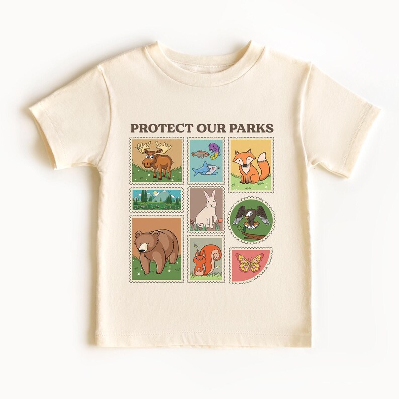 May include: A beige t-shirt with a graphic print of animals and the text "PROTECT OUR PARKS". The graphic features a moose, fish, fox, rabbit, eagle, bear, squirrel, and butterfly.