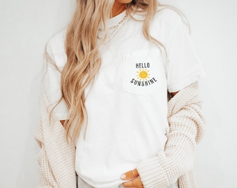 May include: White t-shirt with a pocket featuring a yellow sun and the text "Hello Sunshine".