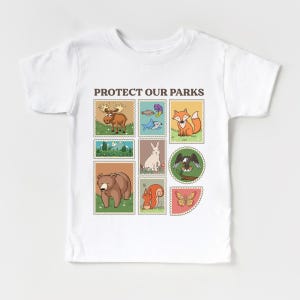 May include: White t-shirt with the text "PROTECT OUR PARKS" printed on the front. The text is surrounded by nine colorful squares, each featuring a different animal or nature scene, including a moose, a fish, a fox, a rabbit, an eagle, a bear, a squirrel, and a butterfly.