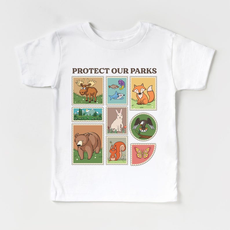 May include: White t-shirt with the text "PROTECT OUR PARKS" printed on the front. The text is surrounded by nine colorful squares, each featuring a different animal or nature scene, including a moose, a fish, a fox, a rabbit, an eagle, a bear, a squirrel, and a butterfly.