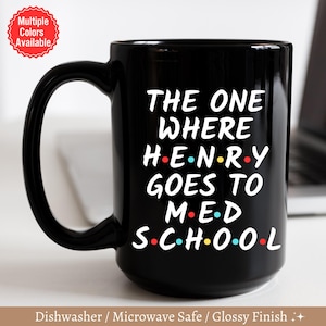 May include: Black coffee mug with white text that reads "The One Where Henry Goes To Med School" with colorful dots replacing the vowels in the words.