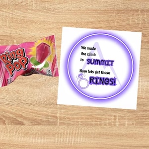 May include: A white card with a purple circle and the text "We made the climb to SUMMIT Now lets get those RINGS!"  A pink Ring Pop candy wrapper is in the background.