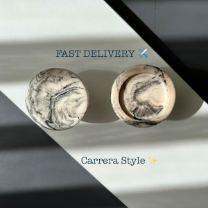 Op de afbeelding: Twee ronde decoratieve objecten in Carrera-stijl met een gemarmerd zwart-wit patroon. Eén is massief, de andere heeft een verzonken midden. De tekst "FAST DELIVERY" en "Carrera Style" zijn ook zichtbaar.