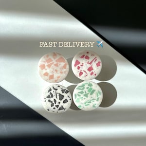 Pode incluir: Quatro objetos decorativos redondos com padrões em estilo terrazzo em rosa, vermelho, preto e verde. O texto "FAST DELIVERY" está acima dos objetos, com um pequeno ícone de avião.