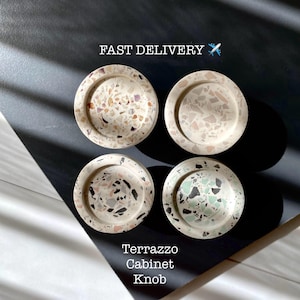 May include: Four round terrazzo cabinet knobs in various colors and patterns. The knobs are made of white concrete with small pieces of colored glass and stone embedded in the surface. The text "Terrazzo Cabinet Knob" is printed below the knobs.
