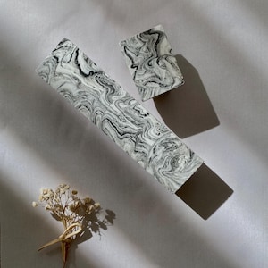 Può includere: Due blocchi decorativi con un motivo marmoreo in tonalità di bianco e nero. I blocchi sono di forma rettangolare e sono disposti su una superficie grigio chiaro.