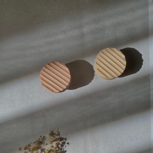 Pode incluir: Dois  copos de apoio redondos, bege e texturizados com um padrão listrado. Um pequeno buquê de flores secas está no canto inferior esquerdo da imagem.