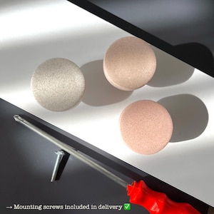 Puede incluir: Tres pomos redondos para armarios en tonos beige y rosa, con superficie texturizada. Tambi&eacute;n se ven un destornillador rojo y un tornillo. El texto dice: "Tornillos de montaje incluidos en la entrega" y "F&aacute;cil de fijar con un destornillador."