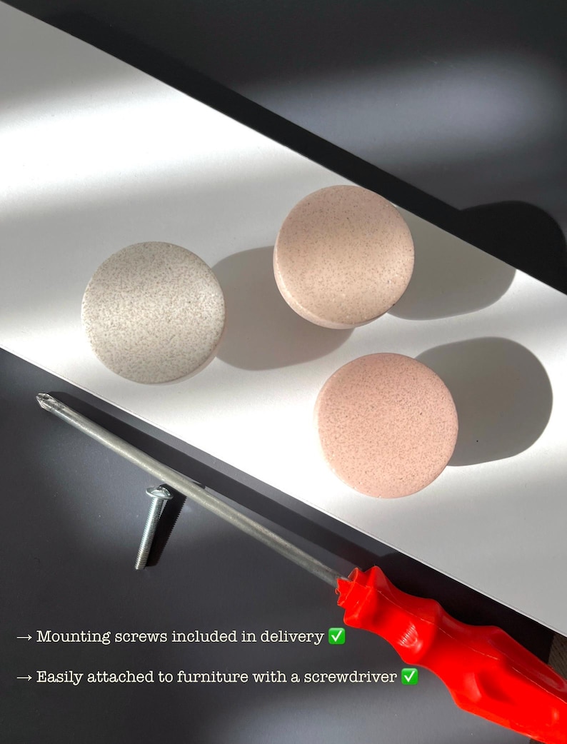 Puede incluir: Tres pomos redondos para armarios en tonos beige y rosa, con superficie texturizada. Tambi&eacute;n se ven un destornillador rojo y un tornillo. El texto dice: "Tornillos de montaje incluidos en la entrega" y "F&aacute;cil de fijar con un destornillador."