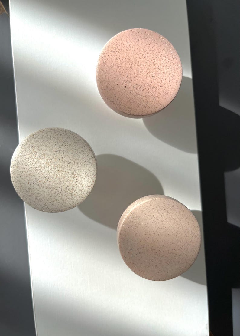 Puede incluir: Tres objetos decorativos redondos y moteados en tonos rosa y beige. Est&aacute;n dispuestos sobre una superficie blanca, con sombras que a&ntilde;aden profundidad. La textura moteada y los colores neutros sugieren un dise&ntilde;o minimalista.