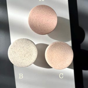 Puede incluir: Tres posavasos redondos y moteados en tonos rosa y blanco roto est&aacute;n dispuestos sobre una superficie blanca. Los posavasos est&aacute;n etiquetados A, B y C. Los posavasos tienen un aspecto texturizado.