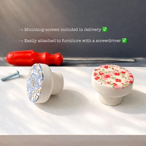 May include: Two ceramic cabinet knobs. One knob features a blue and yellow floral design, the other has a red floral pattern. A red screwdriver and a screw are also visible. The text says, "Mounting screws included in delivery" and "Easily attached to furniture with a screwdriver."