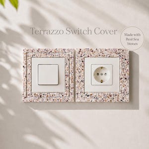 Könnte beinhalten: Ein Terrazzo Switch Cover Set bestehend aus einem Lichtschalter und einer Steckdose, beide eingefasst in ein gesprenkeltes Terrazzo-Material aus echten Meeressteinen. Der Text Terrazzo Switch Cover und Made with Real Sea Stones ist sichtbar.