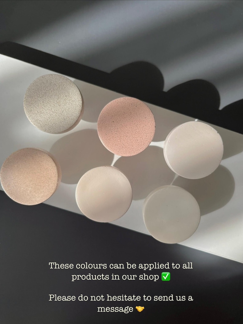 Puede incluir: Seis objetos redondos en tonos neutros, beige, rosa y blanco, dispuestos sobre una superficie blanca. La imagen incluye texto que indica que estos colores est&aacute;n disponibles para todos los productos. Los objetos est&aacute;n espaciados uniformemente y tienen un acabado mate.