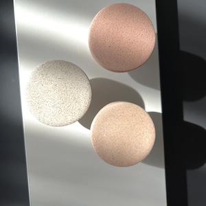 Puede incluir: Tres posavasos redondos y moteados en tonos blanco, rosa y beige. Los posavasos est&aacute;n dispuestos sobre una superficie clara, con sombras. El dise&ntilde;o moteado les da una apariencia texturizada, adecuados para la decoraci&oacute;n del hogar.