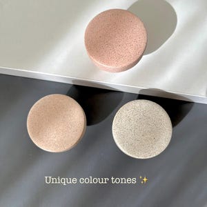 Puede incluir: Tres objetos redondos y moteados en tonos rosa, beige y gris est&aacute;n dispuestos sobre una superficie gris y blanca. El texto "Unique colour tones" es visible. Los objetos parecen decorativos o funcionales.
