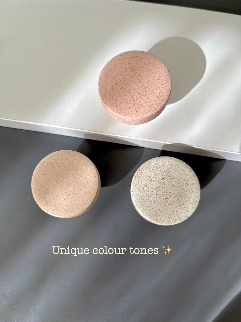 Puede incluir: Tres objetos redondos y moteados en tonos rosa, beige y gris est&aacute;n dispuestos sobre una superficie gris y blanca. El texto "Unique colour tones" es visible. Los objetos parecen decorativos o funcionales.