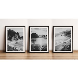 May include: A set of three black and white framed photographs of a rocky coastline with crashing waves. The photos are arranged horizontally on a wooden surface.