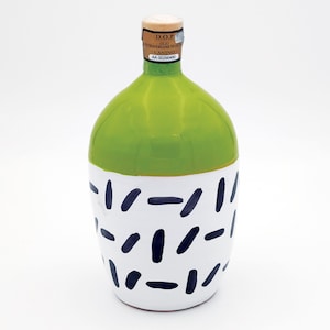 Puede incluir: Una botella de aceite de oliva de cerámica verde y blanca con un patrón geométrico en blanco y negro. La botella tiene una etiqueta que dice "D.O.P. OLIO EXTRAVERGINE DI OLIVA CANINO - AA 00290480".