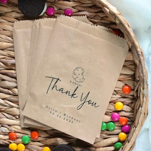 May include: A stack of brown paper bags with a thank you message printed on them. The message includes a cookie graphic and the text "a sweet thank you" and "Olive & Michael 06.22.2025".