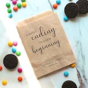 Op de afbeelding: Een bruine papieren zak met de tekst "A sweet ending to a new beginning" en de namen "Hannah & James" en de datum "08.24.26".