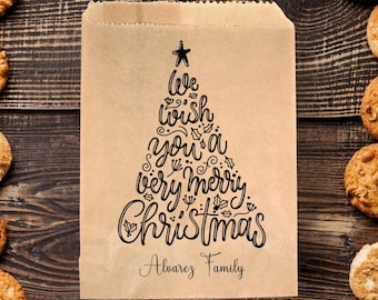 May include: A brown paper bag with a Christmas tree design. The tree is made of the words "We wish you a very merry Christmas" and has a star on top. The bag also has the text "Alvarez Family" at the bottom.