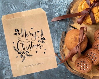 May include: A brown paper gift bag with a black "Merry Christmas" design and the text "ALVAREZ FAMILY". The bag is next to a wooden tray with cookies and a brown ribbon.