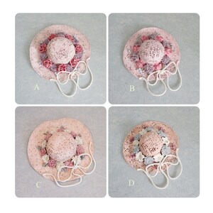 May include: Four pink straw hats with white trim and floral embellishments. Each hat has a different arrangement of flowers and a white ribbon tied around the crown.