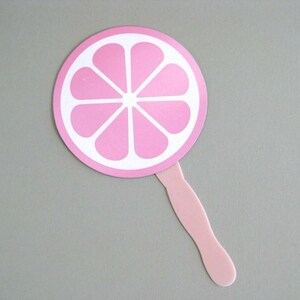 May include: A pink hand fan with a white outline of a pink grapefruit slice.