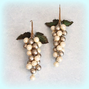 May include: Two decorative grape clusters with pearl-like beads in cream and silver. Each cluster has a brown stem and green leaves, creating a realistic appearance. Ideal for home decor or craft projects.