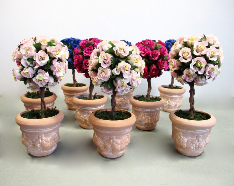 May include: A set of eight small potted topiary trees with pink, red, and blue flowers. The trees are in terracotta pots with a decorative design.