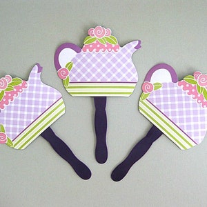 May include: Three purple and green teapots with pink flowers and a checkered pattern on a light gray background. The teapots are attached to purple sticks.