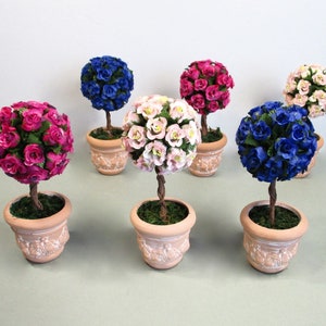 May include: Six miniature topiary trees in terracotta pots. The trees are decorated with artificial pink, blue, and purple roses.