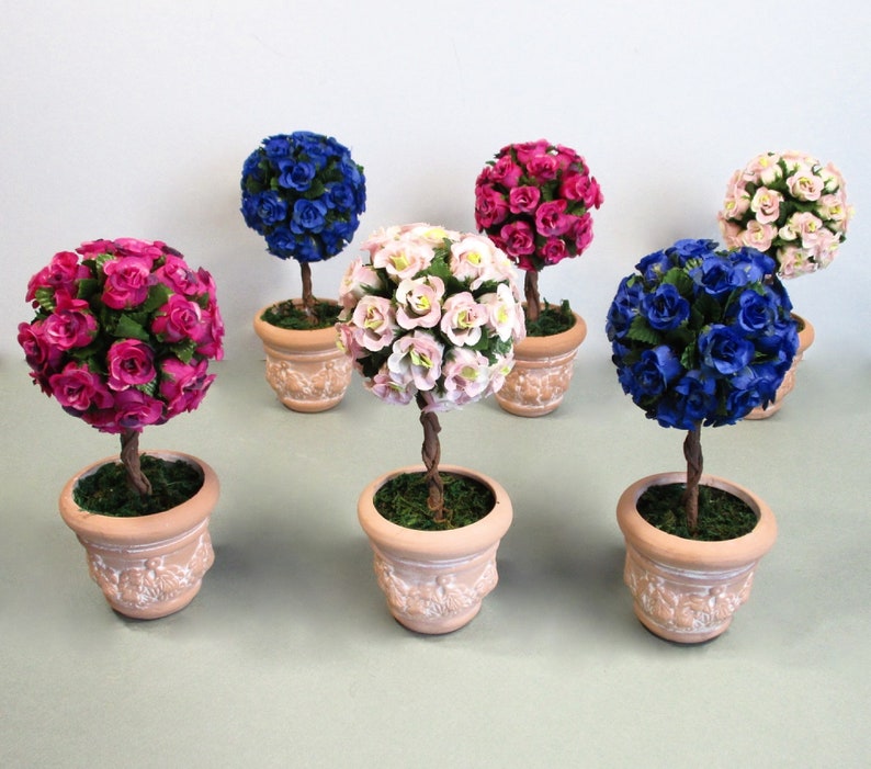 May include: Six miniature topiary trees in terracotta pots. The trees are decorated with artificial pink, blue, and purple roses.